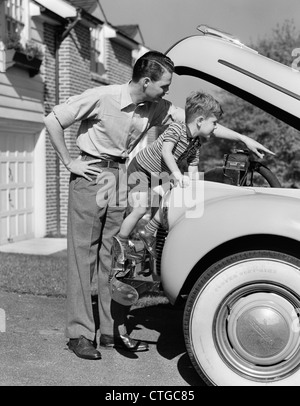 1940ER JAHREN VATER & SOHN ÜBERPRÜFUNG UNTER HAUBE DES AUTOS IN DER EINFAHRT Stockfoto