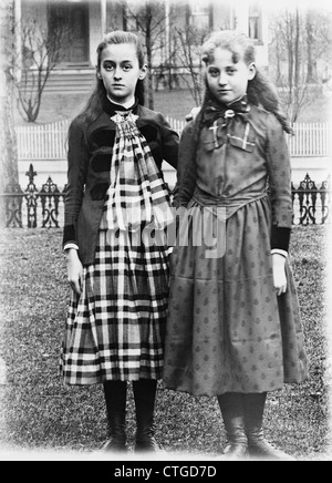 1880ER JAHRE 1900 S 1890ER JAHRHUNDERTWENDE DES JAHRHUNDERTS PORTRÄT ZWEI MÄDCHEN POSIEREN STEHEND ARM IN ARM AUF RASEN HINTERHOF Stockfoto