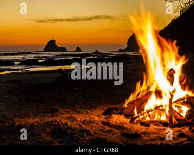 Das glühende Lagerfeuer erhebt sich hoch am Strand bei Sonnenuntergang Stockfoto