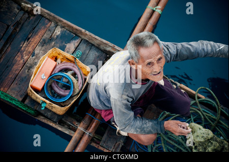 Ein indonesische Fischer in einer traditionellen Piroge Ausleger verkauft Fische an den Koch an Bord eines Segelbootes. Stockfoto