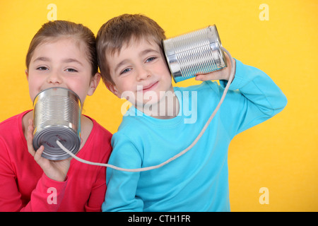 Kinder mit einem Handy anrufen mit Blechdosen auf gelbem Hintergrund Stockfoto