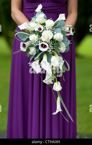 einzelne Brautjungfer in einem lila Kleid hält ein Brautstrauß Stockfoto