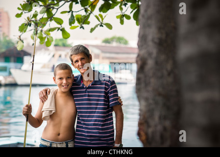 Familienbild mit fröhlicher Junge und Großvater umarmt und lächelt in die Kamera nach dem Angeln in der Nähe von Fluss Stockfoto