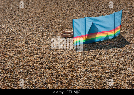 Verdunkelten Sonne Badende liegend auf einem Kiesstrand und bergende hinter einem bunten Windschutz Stockfoto