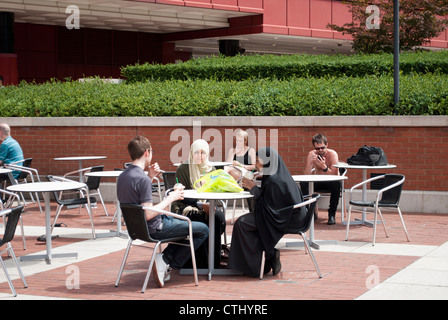 Menschen saßen am Tisch außerhalb der British Library, darunter zwei muslimische Frauen Stockfoto