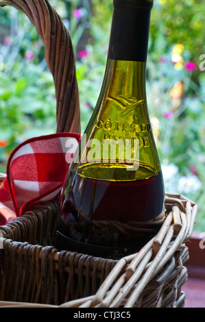 Côtes du Rhône französischer Rotwein Flasche in Weidenkorb in der Nachmittagssonne mit typischen Picknick Serviette und Sommer Garten hinter Stockfoto