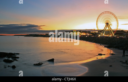 Ein großes Rad mit einer Kirmes in Salthill mit Blick auf die Bucht von Galway, wie die Sonne im Hintergrund. Stockfoto