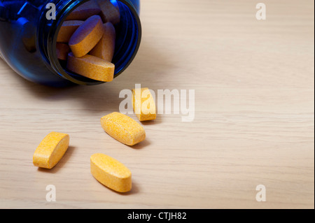 Blaue flasche Gelb vitamin Pillen mit einigen Auslaufen auf den Tisch Stockfoto