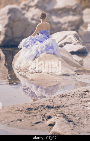 eine Frau im Abendkleid sitzt auf einem Felsen im Wasser Stockfoto