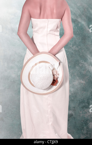 eine Frau in einem weißen Kleid mit einem Strohhut hinter ihrem Rücken Stockfoto