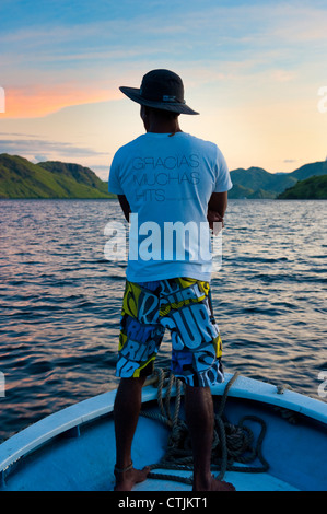 Ein Besatzungsmitglied steht am Bug eines Bootes Reisen durch den Komodo Nationalpark im indonesischen Archipel bei Sonnenuntergang. Stockfoto