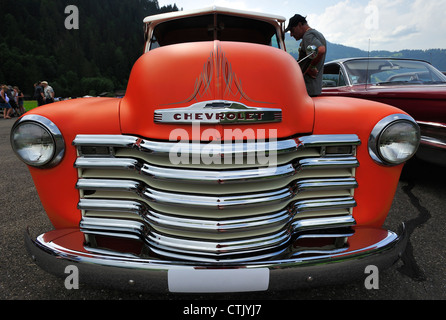 Wide-angle close up of the radiator grille of an old Chevrolet pick-up truck with a spectator looking into the cab Stockfoto