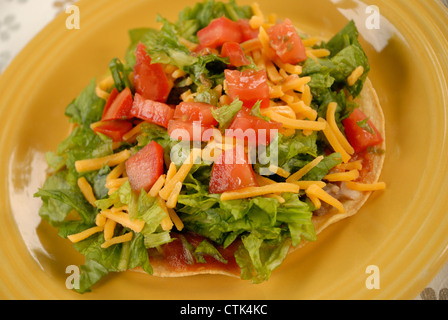 Vegetarische Tostada; Mais-Tortilla mit gebackenen Bohnen, Salat, Käse und Tomaten, mit Taco-Sauce gekrönt. Stockfoto