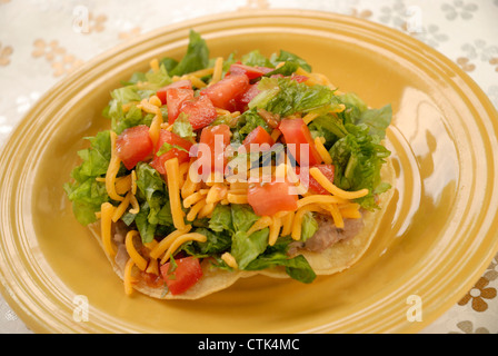 Vegetarische Tostada; Mais-Tortilla mit gebackenen Bohnen, Salat, Käse und Tomaten garniert. Stockfoto