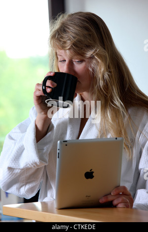 Junge Frau nutzt eine IPad, Tablet-Computer, Surfen im Internet, über Funkverbindung, am Morgen, nach einer Tasse Kaffee Stockfoto