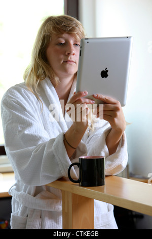 Junge Frau nutzt eine IPad, Tablet-Computer, Surfen im Internet, über Funkverbindung, am Morgen, nach einer Tasse Kaffee Stockfoto