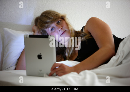 Junge Frau nutzt einen IPad Tablet-Computer in ihrem Schlafzimmer, Nachrichten, lesen, Surfen, Internet, wireless Internet-Anschluss. Stockfoto