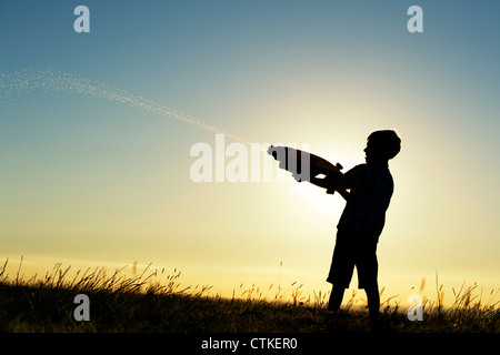 Junge schießen eine Wasserpistole bei Sonnenuntergang. Silhouette. UK Stockfoto