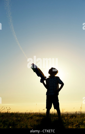 Junge schießen eine Wasserpistole bei Sonnenuntergang. Silhouette. UK Stockfoto