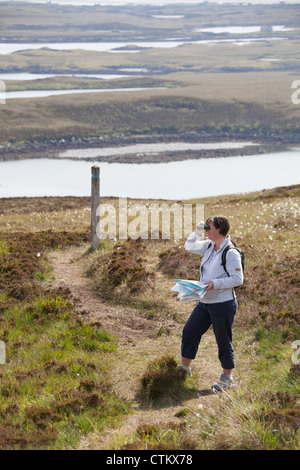 Isle of North Uist, Schottland. Lady Walker überprüfen ihr OS Map auf Beinn Langais mit Loch Langais im Hintergrund. Stockfoto