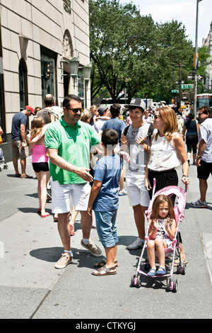 glückliche Familie mit jüngeren jungen Teenager-Sohn & kleine Tochter im Kinderwagen Pause auf 5th Avenue Bürgersteig vor Bergdorf Goodman NY Stockfoto