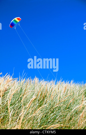 Ein Kite ist gesehen fliegen hinter grasbewachsenen Sanddünen mit einem strahlend blauen Himmel in Camber Sands East Sussex Stockfoto