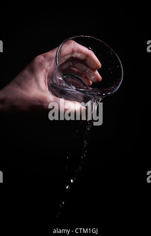 Männer Hand goss Wasser aus einem Glas auf einem schwarzen Hintergrund Stockfoto