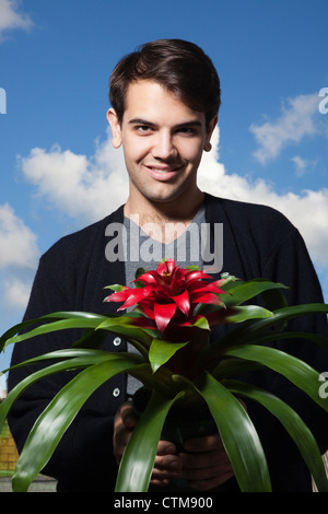Porträt eines lächelnden jungen Mannes mit roten Blumen und grünen Blättern im Vordergrund Stockfoto