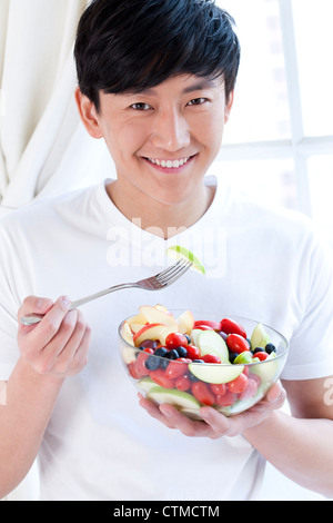 Junger Mann isst Obstsalat Stockfoto