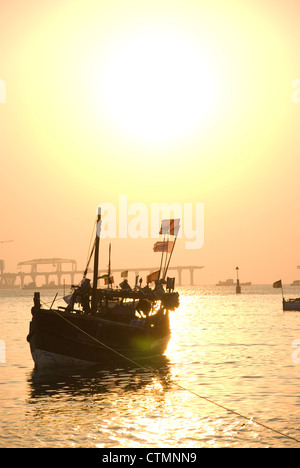 Silhouette einer Fähre während des Sonnenuntergangs - Mumbai, Indien. Bau von Worli Sea Link im Hintergrund Stockfoto