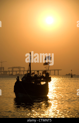 Silhouette einer Fähre und Boot während des Sonnenuntergangs - Mumbai, Indien. Bau von Worli Sea Link im Hintergrund Stockfoto