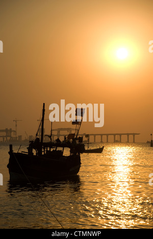 Silhouette einer Fähre und Boot während des Sonnenuntergangs - Mumbai, Indien. Bau von Worli Sea Link im Hintergrund Stockfoto