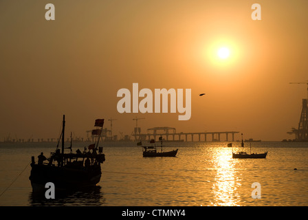 Silhouette von Fähren und Boote während des Sonnenuntergangs - Mumbai, Indien. Bau von Worli Sea Link im Hintergrund Stockfoto