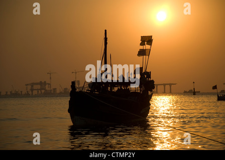 Silhouette einer Fähre während des Sonnenuntergangs - Mumbai, Indien. Bau von Worli Sea Link im Hintergrund Stockfoto