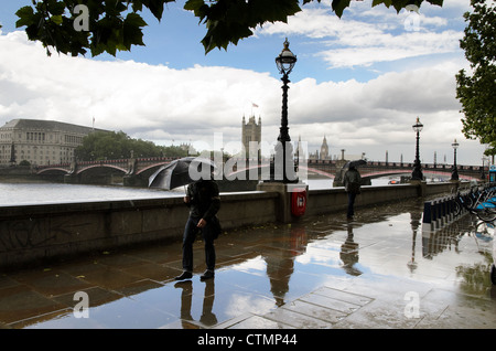 Mann mit Schirm zu Fuß entlang der Albert Embankment - London, England Stockfoto