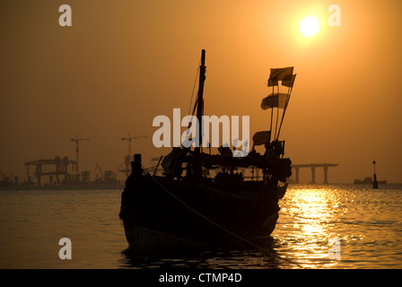 Silhouette einer Fähre während des Sonnenuntergangs - Mumbai, Indien. Bau von Worli Sea Link im Hintergrund Stockfoto