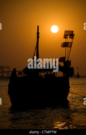 Silhouette einer Fähre während des Sonnenuntergangs - Mumbai, Indien. Bau von Worli Sea Link im Hintergrund Stockfoto