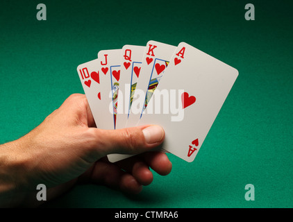 Eines Mannes Hand mit Spielkarten am grünen Tisch. Ein Royal Flush in Herzen in das Spiel von Poker Stockfoto