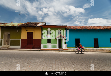 Mann fährt Fahrrad vorbei an bunten Häuserfassaden auf Kopfsteinpflaster Straße im historischen Viertel in Granada, Nicaragua. Stockfoto