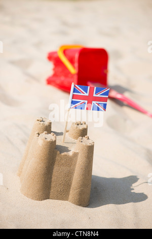 Union Jack-Flagge in eine Sandburg neben einem Childs Eimer und Schaufel an einem Strand. Brunnen neben das Meer. Norfolk, England Stockfoto