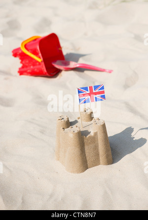 Union Jack-Flagge in eine Sandburg neben einem Childs Eimer und Schaufel an einem Strand. Brunnen neben das Meer. Norfolk, England Stockfoto