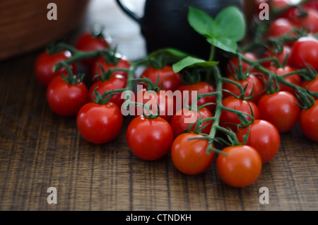 Einige Kirschtomaten auf dunkle Eiche Brett mit Tonkrug im Hintergrund. Stockfoto