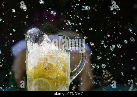 Gießen Sie Wasser und Splahing in Glaskrug voller Zitronen an sonnigen Tag. Stockfoto