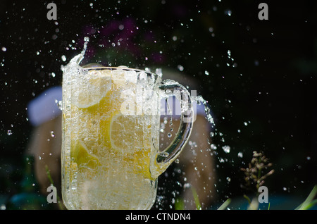 Gießen Sie Wasser und Splahing in Glaskrug voller Zitronen an sonnigen Tag. Stockfoto