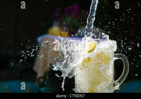 Gießen Sie Wasser und Splahing in Glaskrug voller Zitronen an sonnigen Tag. Stockfoto