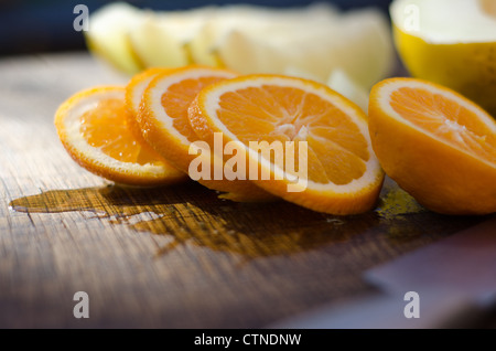 Scheiben von frisch geschnittenen Orange auf einem Eiche Board mit aus Fokus Melone im Hintergrund. Stockfoto