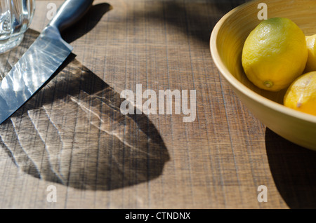 Eine Schüssel mit Zitronen neben dem Messer und dem Krug auf eine Eiche Brett bereit, an einem Sommertag in Limonade zu machen. Stockfoto