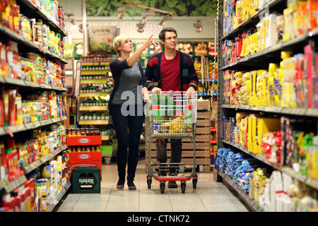 Ein junges Paar in einem großen Supermarkt, mit einem Wagen, zu Fuß durch die Gänge mit Regale voller Lebensmittel einkaufen. Stockfoto