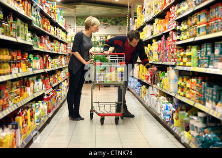 Ein junges Paar in einem großen Supermarkt, mit einem Wagen, zu Fuß durch die Gänge mit Regale voller Lebensmittel einkaufen. Stockfoto