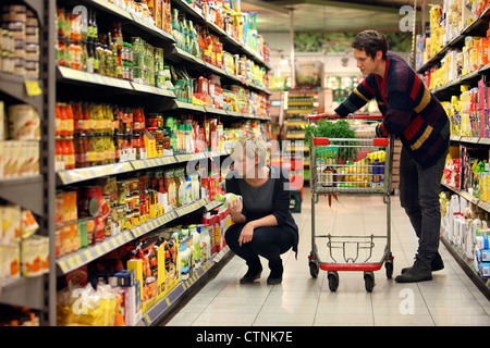 Ein junges Paar in einem großen Supermarkt, mit einem Wagen, zu Fuß durch die Gänge mit Regale voller Lebensmittel einkaufen. Stockfoto